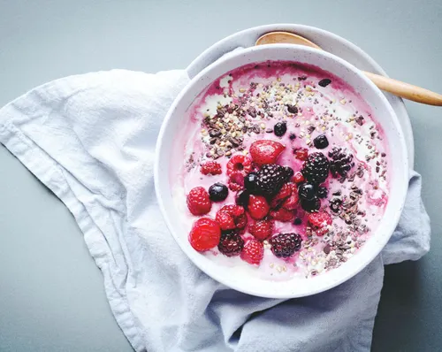 A bowl of yogurt topped with a blueberry and mint leaf.